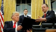 U.S. President Donald Trump hands Chief of Staff Reince Priebus (R) an executive order that directs agencies to ease the burden of Obamacare, after signing it in the Oval Office in Washington, U.S. January 20, 2017. REUTERS/Jonathan Ernst 
