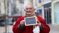 Francois Dore, 83, retired, holds a blackboard with the word 