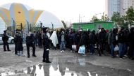 French anti-riot police CRS officers stand guard by migrants and refugees queueing by the migrant camp at Porte de la Chapelle during the evacuation of a makeshift camp near La Chapelle, in Paris, on May 9, 2017, one of several camps sprouting up around t