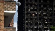 A man stands on his balcony in front of the burnt out shell of the Grenfell apartment tower block in North Kensington, London, Britain, June 17, 2017. REUTERS/Hannah McKay
