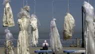 A veiled woman sitting on a bench near an installation of wedding dresses by Lebanese artist Mireille Honein and Abaad NGO at Beirut's Corniche, denouncing the article 522 of Lebanon's penal code allowing rapists who marry their victims to go free, in thi