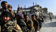 Kurdish fighters of the Syrian Democratic Forces (SDF) ride in the back of a truck passing damaged buildings in Raqa on October 20, 2017, after a Kurdish-led force expelled the Islamic State group from the northern Syrian city.  AFP / Bulent Kilic