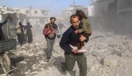 Syrians make their way through debris following a reported air strike in the rebel-held town of Beit Sawa, in the eastern Ghouta region on the outskirts of the capital Damascus, on December 3, 2017. / AFP / Amer ALMOHIBANY