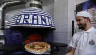 A Neapolitan pizza maker poses next to the oven with a pizza celebrating the Unesco decision to make the art of Neapolitan 
