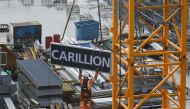 A worker guides down a sign showing the name of liquidated British construction and outsourcing group carillion after it was taken down off a construction crane on a building site in the City of London on January 23, 2017. / AFP / Daniel SORABJI