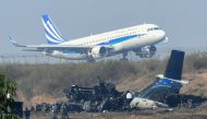 An airplane takes off at the international airport in Kathmandu on March 13, 2018, near the wreckage of a US-Bangla Airlines plane that crashed on March 12. AFP / PRAKASH MATHEMA
