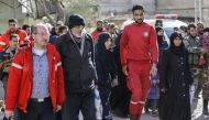 Members of the Syrian Red Crescent escort evacuated civilians from the rebel-held Eastern Ghouta enclave into the government side of the Wafideen checkpoint on the outskirts of the Syrian capital Damascus on March 14, 2018. / AFP / LOUAI BESHARA
