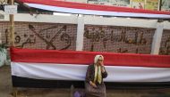 A woman sits outside a polling station decorated with long pieces of cloth depicting the colours of the Egyptian flag in the capital Cairo's central Al-Malek al-Saleh district on March 25, 2018 ahead of the vote scheduled for the following day. AFP / Moha