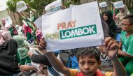 A child holds up a placard that reads 'pray for Lombok' during an earthquake evacuation drill in Medan, on the western Indonesian island of Sumatra on August 8, 2018. / AFP / IVAN DAMANIK