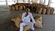A farmer smokes while sitting on sacks of paddy crops as he waits for customers in Sanand village on the outskirts of Ahmedabad, November 15, 2016. Reuters