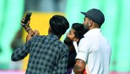 Indian cricket captain Virat Kohli (R) poses for a selfie with fans, as they invaded the field, during the first day's play of the first Test cricket match between India and West Indies at the Saurashtra Cricket Association stadium in Rajkot on October 4,