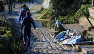 People pass on November 4, 2018 by damages on a flooded road near a house where nine people of the same family died after a small river burst its banks in Casteldaccia near Palermo on the southern Italian island of Sicily.  AFP / Alessandro FUCARINI