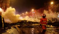 A yellow vest (Gilets Jaune) protestor looks on as a firefighter walks amongst extinguished burning material near The Arc de Triomphe on the Champs Elysees in Paris, on November 24, 2018, during a rally by yellow vest protestors against rising oil prices 