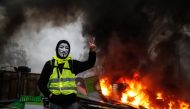 A protester wearing a Guy Fawkes mask makes the victory sign near a burning barricade during a protest of Yellow vests (Gilets jaunes) against rising oil prices and living costs, on December 1, 2018 in Paris. / AFP / Abdulmonam EASSA