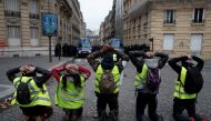 Protesters wearing yellow vests kneel in front French riot police near the Champs-Elysees Avenue at a demonstration by the 