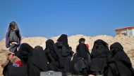 Women wearing niqabs (full face veils) wait as men are being screened by members of the Syrian Democratic Forces, while civilians flee from the battered Islamic State-held holdout of Baghouz in the eastern Syrian province of Deir Ezzor into a nearby area 