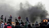 Palestinian protesters use slingshots to hurl rocks as smoke billows from tires burning during clashes with Israeli forces following a demonstration marking the first anniversary of the 