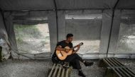  A man plays the guitar at an unofficial camp outside the refugee camp of Moria on the Greek island of Lesbos, on March 19, 2019. AFP / Aris Messinis 