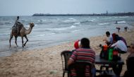 A Palestinian man rides a camel as people sit on a beach on a hot day in Gaza City, July 12, 2017. Reuters/Mohammed Salem