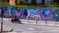 A man rides a motorbike past a graffiti reading 