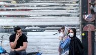 An Iranian youth talks on the phone as he watches women wearing protective masks walk by on a street of the capital Tehran, on May 09, 2020, amid the novel coronavirus pandemic. / AFP / ATTA KENARE