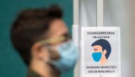 A man wearing a face mask stands next to a sign reading 