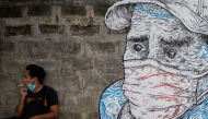 A man smokes a cigarette next to a mural of a man wearing a protective mask amid the coronavirus disease (COVID-19) outbreak in Quezon City, Metro Manila, Philippines, July 30, 2020. REUTERS/Eloisa Lopez
