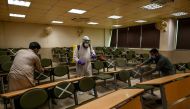 A worker wearing a Personal Protective Equipment (PPE) suit (C) sprays disinfectant while other workers tag cross signs on chairs for social distancing at the Capital University of Science and Technology in Islamabad on September 10, 2020, following the g