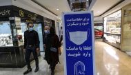 Iranians walk next to a sign advising people to wear masks on their way to shop in Tajrish square in the capital Tehran on November 1, 2020, amid the novel coronavirus pandemic crisis. / AFP / ATTA KENARE
