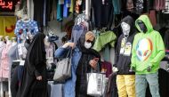 A woman, mask-clad due to the COVID-19 coronavirus pandemic, browses a phone as she walks past a shop along a street in Iran's capital Tehran on November 8, 2020. / AFP / ATTA KENARE