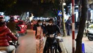 A woman (L) wearing a facemask adjusts her helmet along a street in Hanoi on December 1, 2020, a day after Vietnam reported its first local transmission case of Covid-19 in nearly three months. AFP / Manan Vatsyayan 