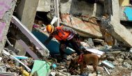 An Indonesian police officer with a K9 unit sniffer dog search for victims among the ruins of a hospital building collapsed following an earthquake in Mamuju, West Sulawesi province, Indonesia, January 18, 2021 in this photo taken by Antara Foto. Antara F