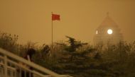 A pedestrian walks near a Chinese flag amid a duststorm in Beijing, China April 15, 2021. Reuters/Tingshu Wang