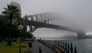 A woman jogs along the waterfront past the Sydney Harbour Bridge, seen shrouded in fog, during a lockdown to curb the spread of a coronavirus disease (COVID-19) outbreak in Sydney, Australia, June 30, 2021. REUTERS/Loren Elliott
