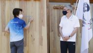 Tokyo 2020 President Seiko Hashimoto signs her autograph on a mural set up to wish for a truce in warring areas of the world during the Olympic Games while IOC President Thomas Bach looks on, at the athletes' village in Tokyo, Japan July 19, 2021. Kyodo/v