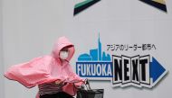 A woman wearing a protective mask and a rain coat, amid the coronavirus disease (COVID-19) outbreak, rides a bicycle in the rain in Fukuoka, Fukuoka Prefecture, Japan, August 17, 2021. REUTERS/Kim Kyung-Hoon