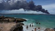 People enjoy the beach near the smoke of a fire over fuel storage tanks that exploded near Cuba's supertanker port in Matanzas, Cuba, August 6, 2022. REUTERS/Alexandre Meneghini