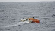 This handout photo taken and released on January 25, 2023 by the 7th Regional Coast Guard headquarters of the Japan Coast Guard shows Coast Guard personnel (centre L) checking on a lifeboat (centre R-in orange) from the Jin Tian cargo ship floating at sea. (Photo by Handout / Japan Coast Guard / AFP)
