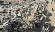 An aerial view shows a tractor working on removing debris from a collapsed building in the Syrian rebel-held town of Jindayris on February 15, 2023, following the February 6 earthquake that hit Turkey and Syria. (Photo by Omar Haj Kadour / AFP)