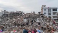 A family sit in front of their former house, destroyed after the 7.8-magnitude earthquake, in Adiyaman, Turkiyes, on March 22, 2023. (Photo by Bulent Kilic / AFP)