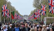 People walk beneath flags of the Union and Commonwealth along The Mall, towards Buckingham Palace, in central London, on April 30, 2023 ahead of the coronation ceremony of Charles III and his wife, Camilla, as King and Queen of the United Kingdom and Commonwealth Realm nations, on May 6, 2023. (Photo by JUSTIN TALLIS / AFP)