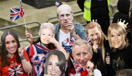 Well-wishers wearing masks of members of the Royal Family wait along the route of the 'King's Procession' (Photo by Loic Venance / AFP)