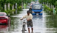 A man pushes a bicycle down a road closed due to flooding at Koshigaya, Saitama Prefecture on June 3, 2023. (Photo by JIJI Press / AFP) 