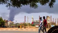 Men walk down a street in Khartoum on June 8, 2023, as smoke rises from behind buildings amid continuing fighting between the army and paramilitary forces. Photo by AFP