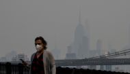 A person wearing a face mask walks before the Empire State Building during heavy smog in New York on June 6, 2023. (Photo by Angela Weiss / AFP)