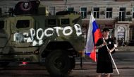 A man holds the Russian national flag in front of a Wagner group military vehicle with the sign read as 