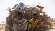 Migrants from sub-Saharan African countries who claim to have been abandoned in the desert by Tunisian authorities, shield themselves from the scorching summer heat in an uninhabited area near the border town of Al-Assah on July 16, 2023. (Photo by Mahmud Turkia / AFP)
