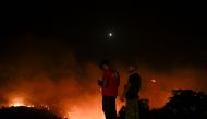 People watch the fires near the village of Malona in the Greek island of Rhodes on July 23, 2023. (Photo by Spyros Bakalis / AFP)