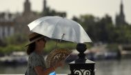 A woman uses an umbrella and a fan to protect herself from the sun and the high temperature in Seville on August 7, 2023. (Photo by Cristina Quicler / AFP)