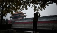 A woman takes a picture along the moat outside the Forbidden City in Beijing on November 21, 2023. Photo by WANG Zhao / AFP